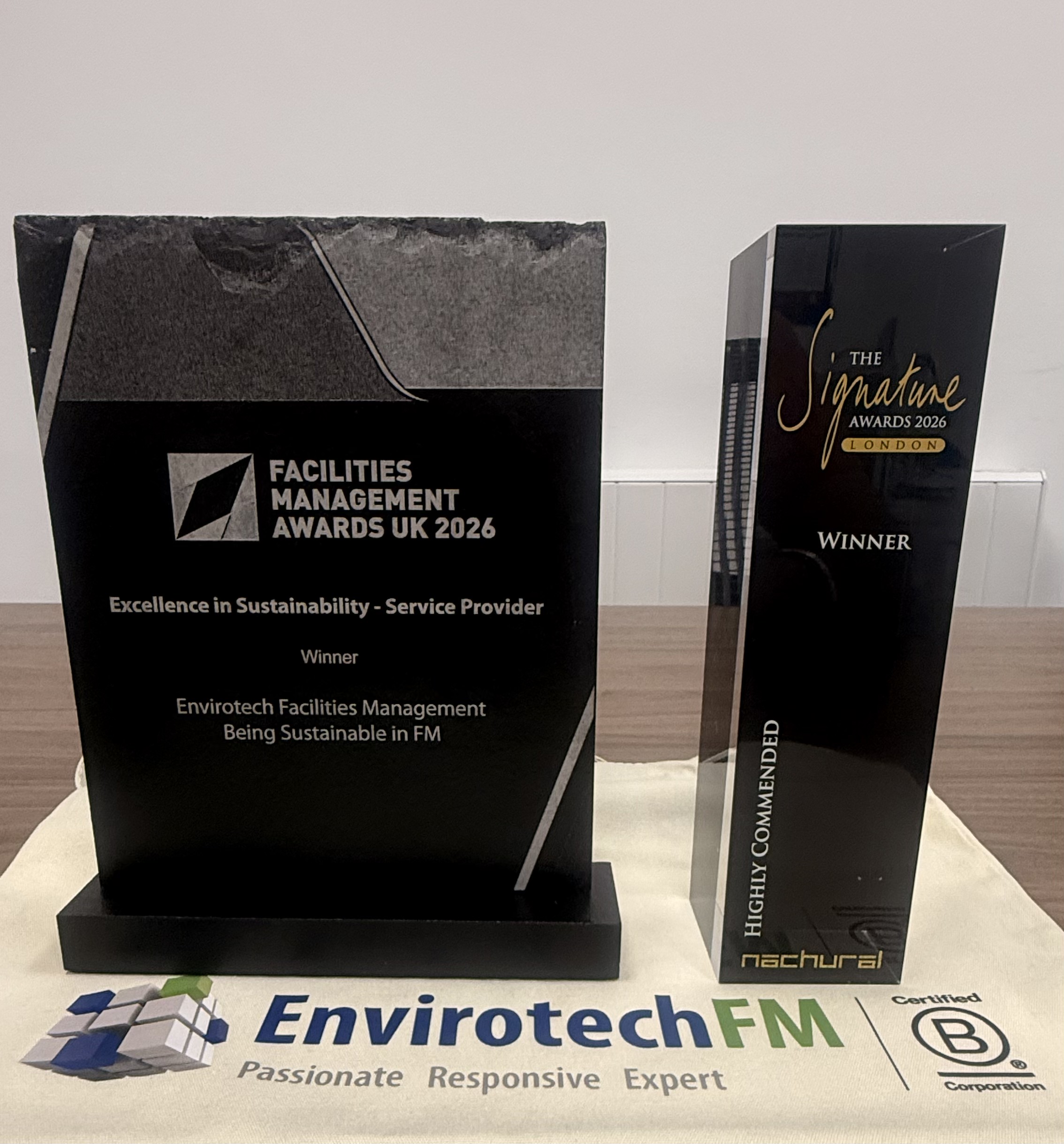 The Facilities Management Awards UK 2026 and Signature Awards 2026 trophies on an Envirotech FM banner